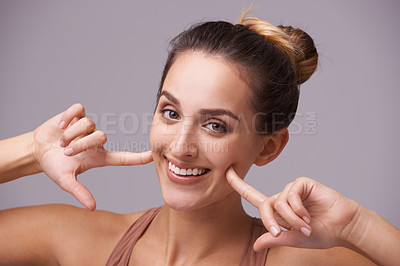 Buy stock photo Portrait, smile and woman pointing at cheeks in studio isolated on purple background. Face, hands on skin or fingers of happy girl, natural model or beauty of person with gesture of facial expression