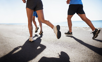 Buy stock photo People, legs and running at beach for cardio, fitness or outdoor workout together on asphalt or road. Closeup of athletic group or runners in sports, teamwork or training exercise by the ocean coast