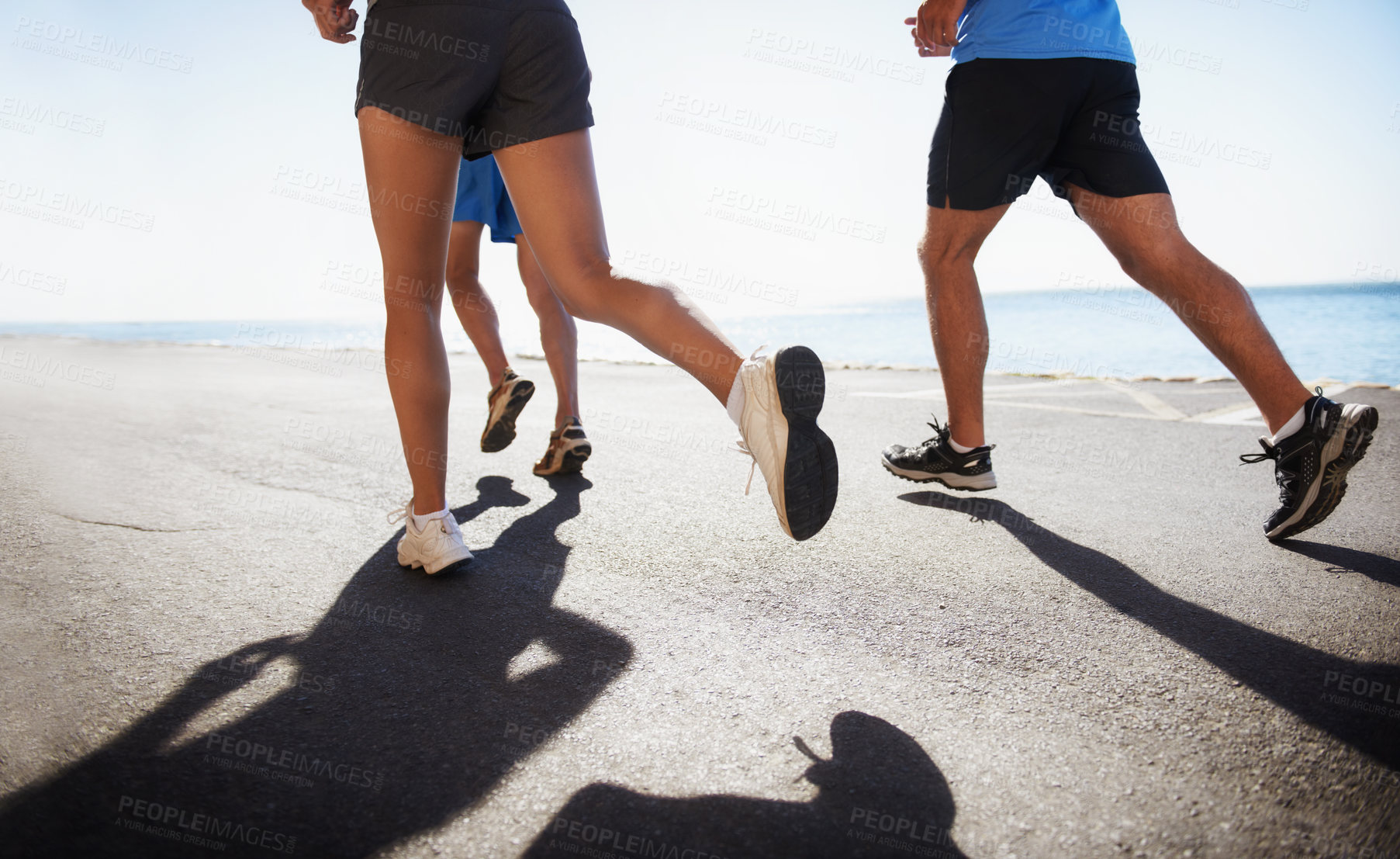 Buy stock photo People, legs and running at beach for cardio, fitness or outdoor workout together on asphalt or road. Closeup of athletic group or runners in sports, teamwork or training exercise by the ocean coast