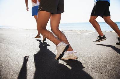 Buy stock photo People, team and legs running at beach for cardio, fitness or outdoor workout together on asphalt or road. Closeup of athletic group or runners in sports or training exercise by the ocean coast