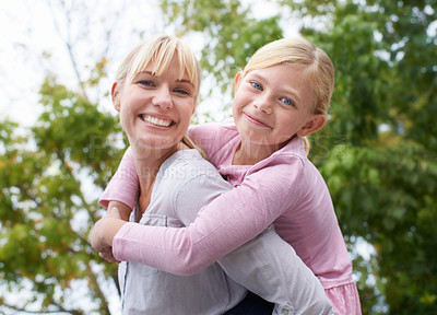 Buy stock photo A happy young mother givign her daughter a piggyback ride in the park