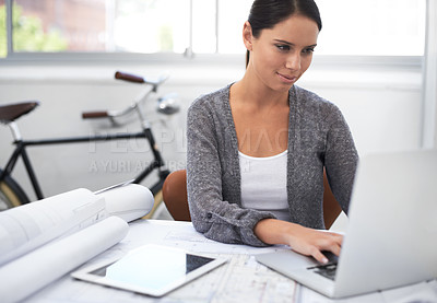 Buy stock photo Shot of a young female designer working at her laptop with a bicycle in the background