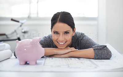 Buy stock photo Shot of a young architect resting on some blueprints and looking at a piggybank