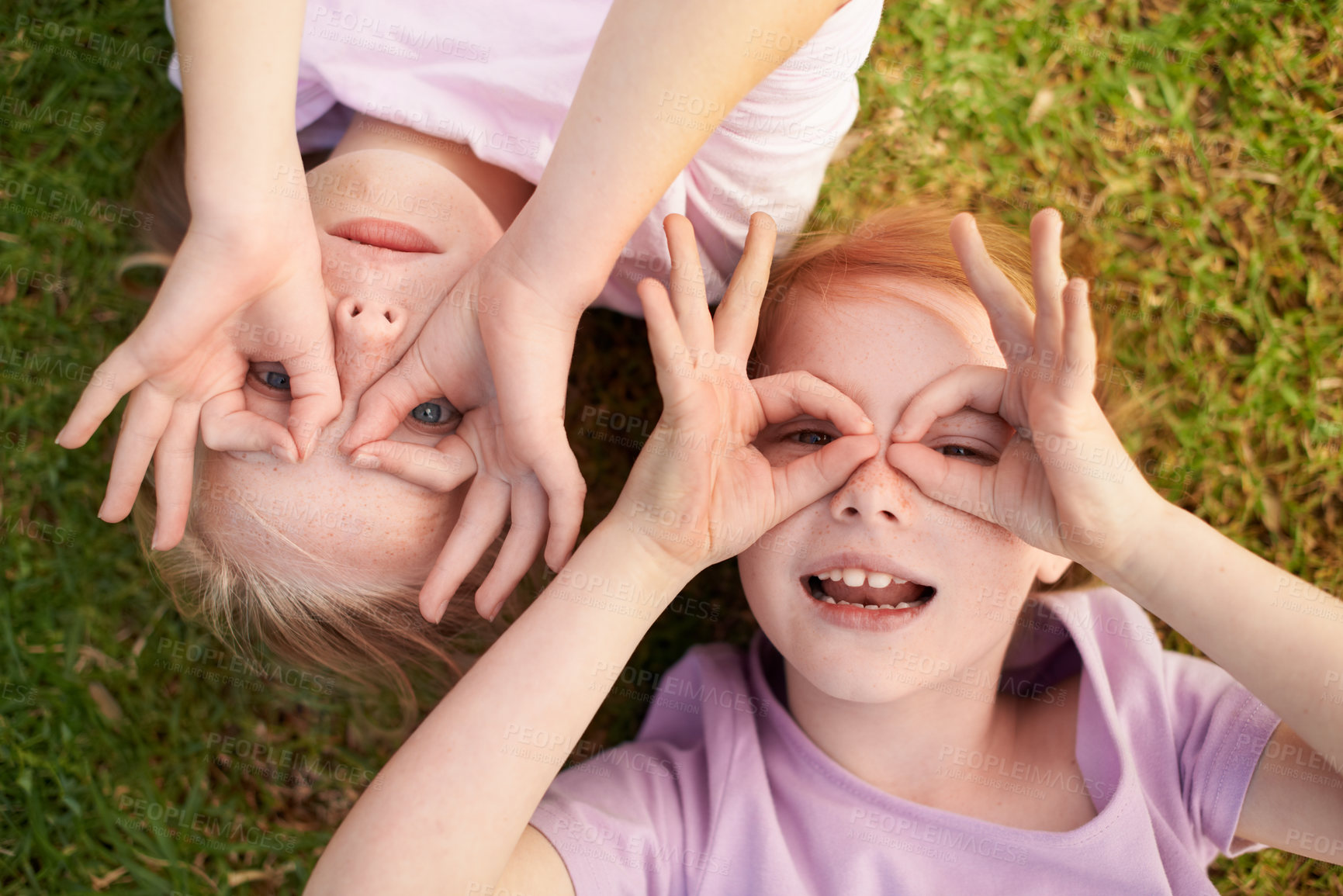 Buy stock photo Two little girls lying on their backs making circles around their eyes with their hands
