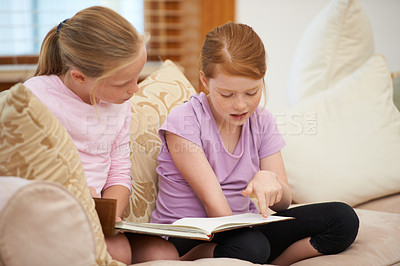 Buy stock photo Sisters, sofa or kids reading book for learning, language development or studying literacy together. Education, children or girl siblings in home for storytelling, hobby or knowledge of literature