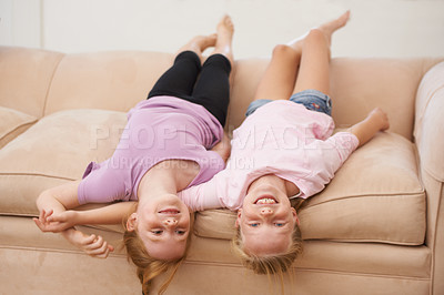 Buy stock photo Girl children, sisters and upside down on couch, bonding for love and care at family home, trust and support. Friends, portrait and time together in lounge, playful and silly with happiness and smile