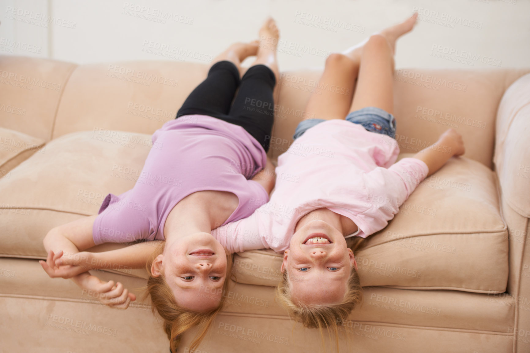 Buy stock photo Girl children, sisters and upside down on couch, bonding for love and care at family home, trust and support. Friends, portrait and time together in lounge, playful and silly with happiness and smile