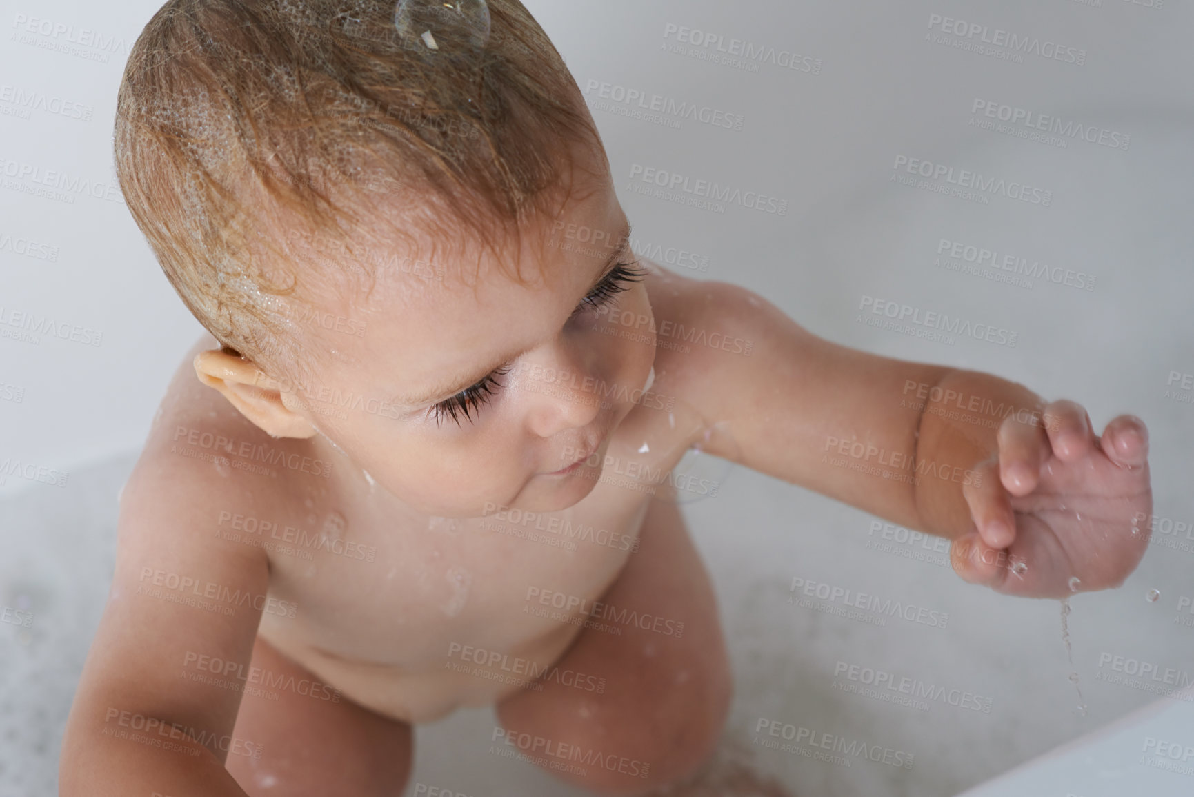 Buy stock photo Baby, child and play with bubbles in bath of water for morning routine, skincare and wellness at home from above. Boy, kid and cleaning in tub with soap, foam and bathroom for fun, hygiene or washing