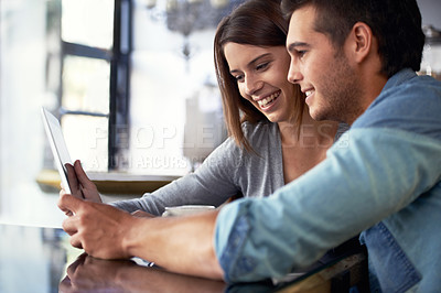 Buy stock photo Shot of a young couple looking at a digital tablet while sitting in a cafe