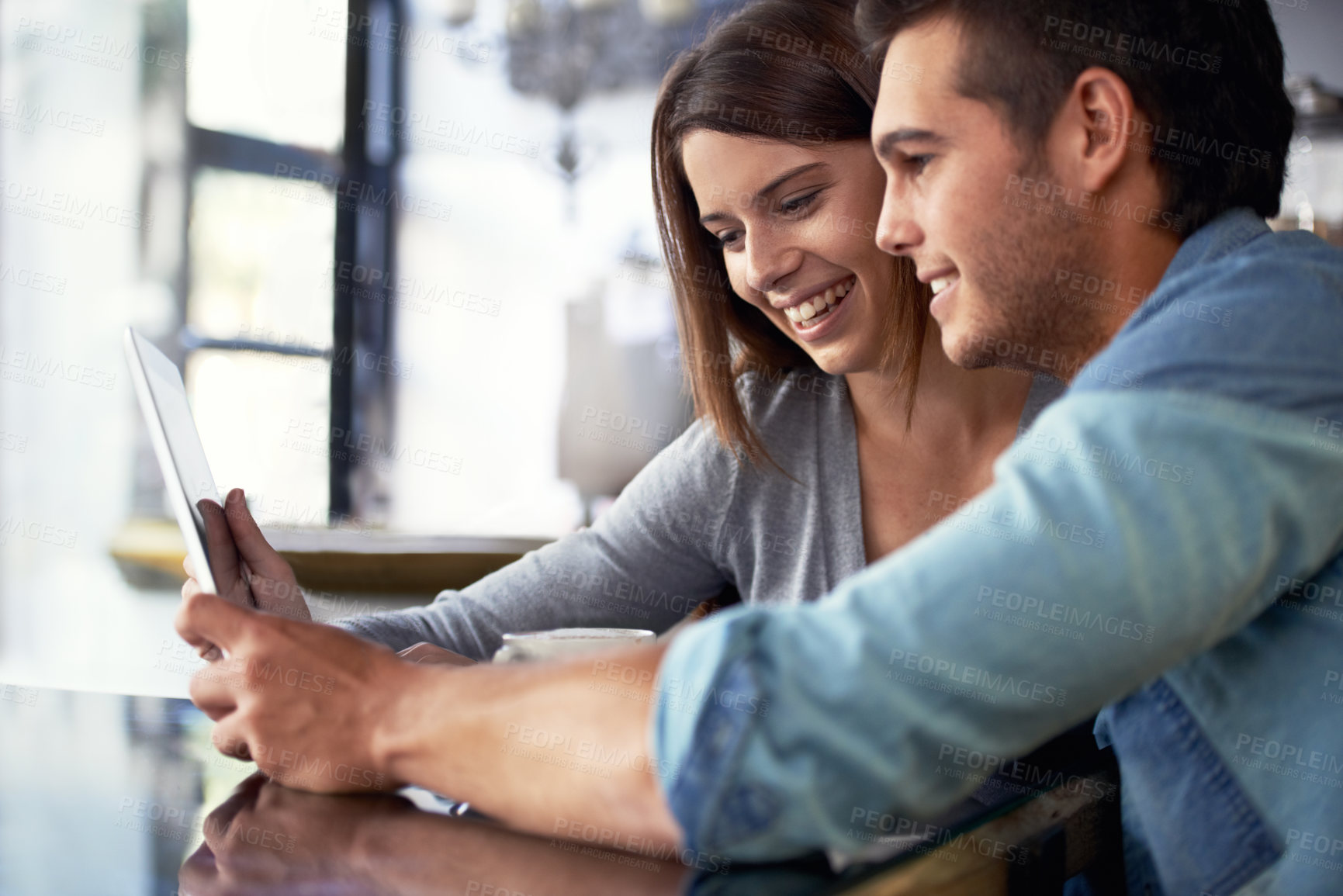 Buy stock photo Shot of a young couple looking at a digital tablet while sitting in a cafe