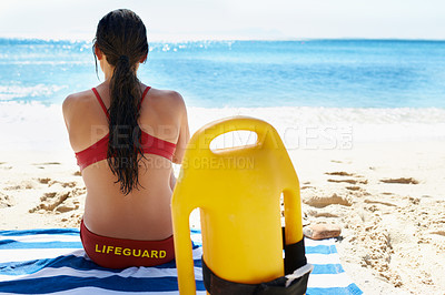 Buy stock photo Beach, lifeguard and back of woman relaxing on the sand for watching on island job with sunshine. Travel, safety and female person with equipment on a towel for career by the shore with ocean or sea.