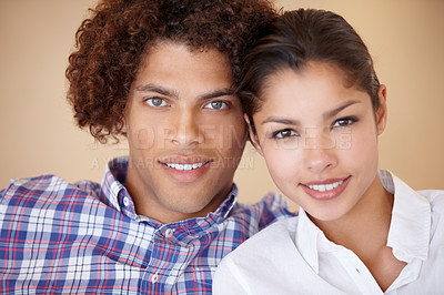 Buy stock photo Studio portrait of a happy young ethnic couple sitting side by side smiling at the camera