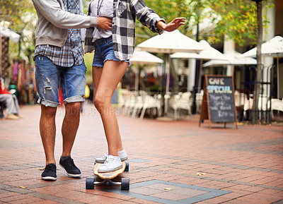 Buy stock photo Skateboard, legs and couple of friends teaching partner how to ride, exercise lesson or training in urban city. Fun activity, cardio fitness and feet of people helping, support and coaching to skate 