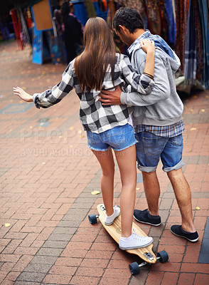 Buy stock photo Couple, skateboarding and teaching in city, back and excited to learn together and romantic relationship. Cape town, fun and hobby with boyfriend and girlfriend in street, helping and dating