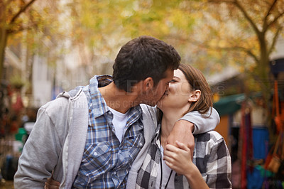 Buy stock photo An affectionate young couple kissing as they walk down the street