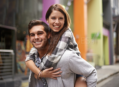 Buy stock photo A young guy smiling while piggybacking his girlfriend out in the street