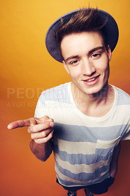 Buy stock photo Portrait, hipster and man with fashion, pointing and confident guy on an orange studio background. Person, hand gesture and model with stylish clothes, hat and casual outfit with aesthetic and trendy