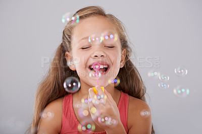 Buy stock photo Happy, little girl and blowing bubbles in studio by toy, cute and fun games for hand eye coordination. Child, eyes closed and play with bubble wand, childhood development and smile by gray background
