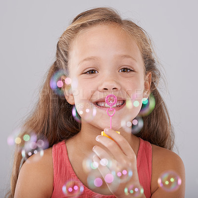 Buy stock photo Portrait, kid and blowing bubbles in studio by toy, happiness and fun games for hand eye coordination. Little girl, face and learning to play on soap wand, development and sweet by gray background