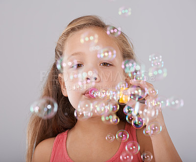 Buy stock photo Portrait, little girl and blowing bubbles in studio by toy, cute and fun games with soap liquid. Child, face and learning to play with bubble wand, childhood development and sweet by gray background