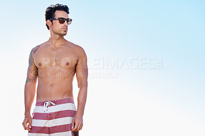 Buy stock photo Waist up shot of a young man in swim trunks against a blue sky