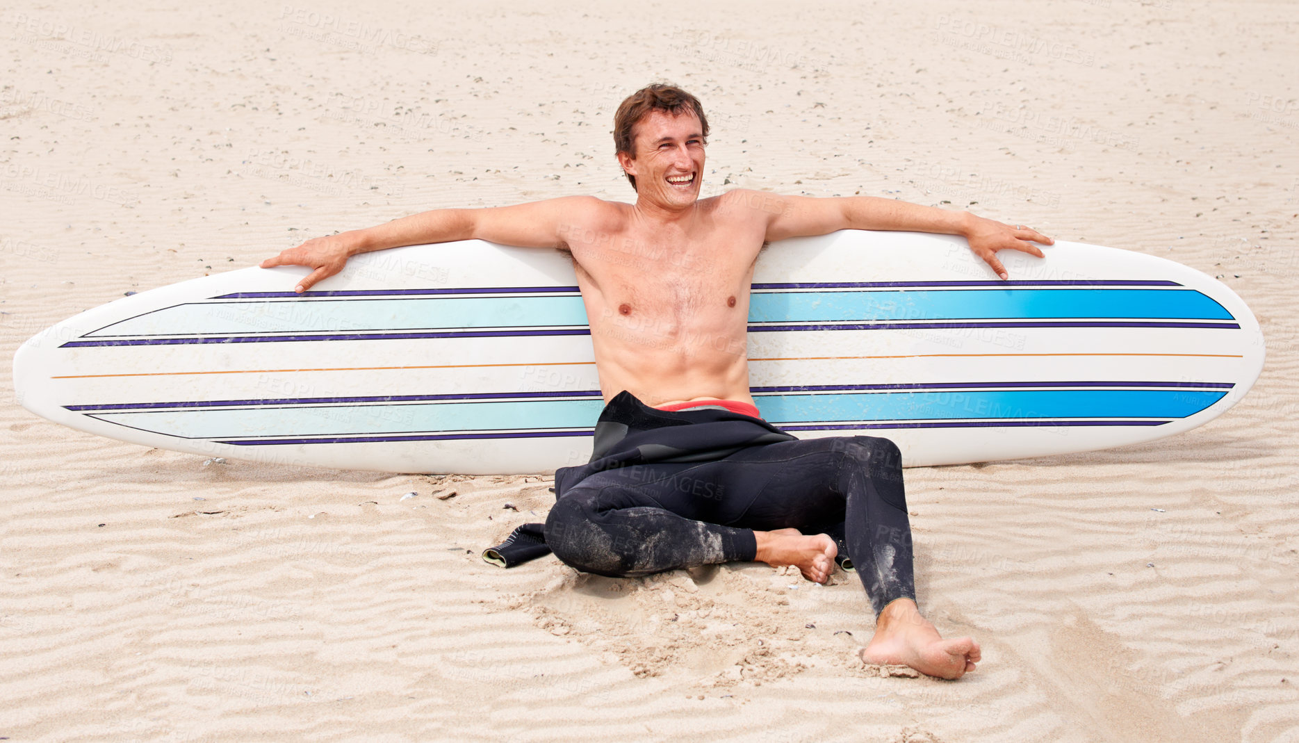 Buy stock photo Relax, vision and laughing man with surfboard on beach in wetsuit for sports, travel or fitness. Thinking, smile and body of young surfer on sand by ocean or sea for break from training and exercise