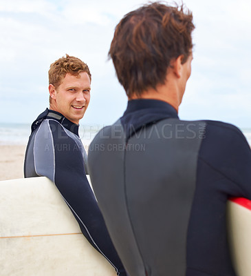 Buy stock photo Two young surfers standing on the beach with the ocean in the background