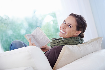 Buy stock photo A relaxed young woman reading an engrossing novel on her couch
