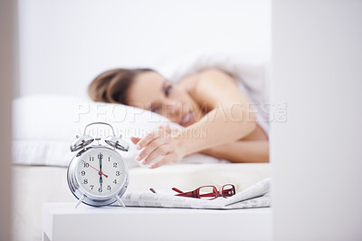 Buy stock photo A young woman waking up and reaching over to her alarm clock
