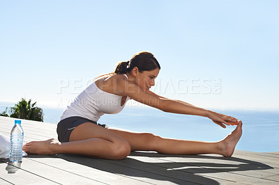 Buy stock photo A young woman stretching on the pier before a workout