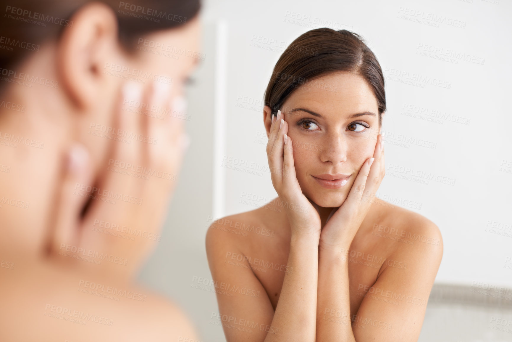 Buy stock photo A gorgeous young woman looking at her reflection in the mirror with her hands on her face