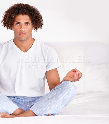 Buy stock photo Cropped portrait of a handsome young ethnic male sitting calmly on a bed and meditating