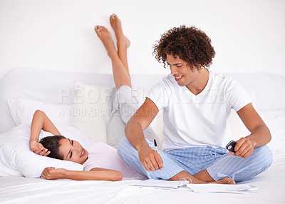 Buy stock photo Shot of a happy young ethnic couple sitting on their bed writing something down