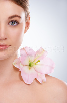 Buy stock photo Cropped studio portrait of half of a model's face with a flower on her bare shoulder