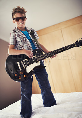 Buy stock photo Smile, playing and kid with guitar on bed for music lesson with sunglasses at modern home. Fun, rockstar and young boy child learning with electric string instrument in bedroom for hobby at house.