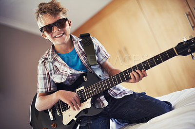 Buy stock photo Smile, playing and child with guitar on bed for music lesson with sunglasses at modern home. Fun, rockstar and young boy kid learning with electric string instrument in bedroom for hobby at house.