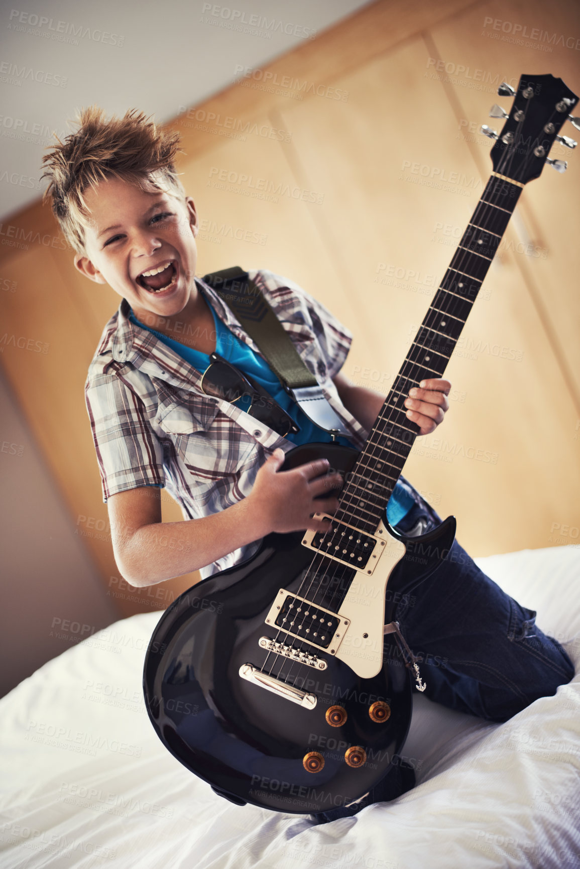 Buy stock photo Happy, portrait and child with guitar on bed for music lesson or practice at modern home. Fun, rockstar and young boy kid playing electric string instrument for concert in bedroom for hobby at house.