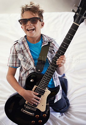 Buy stock photo Happy, playing and boy kid with guitar on bed for music lesson with sunglasses at modern home. Fun, rockstar and young child learning with electric string instrument in bedroom for hobby at house.