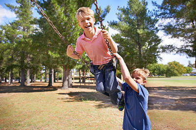 Buy stock photo A young boy enjoying the swings on the playground with friend