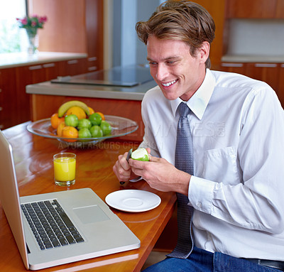 Buy stock photo A young man sitting in the kitchen with his laptop and enjoying a light breakfast