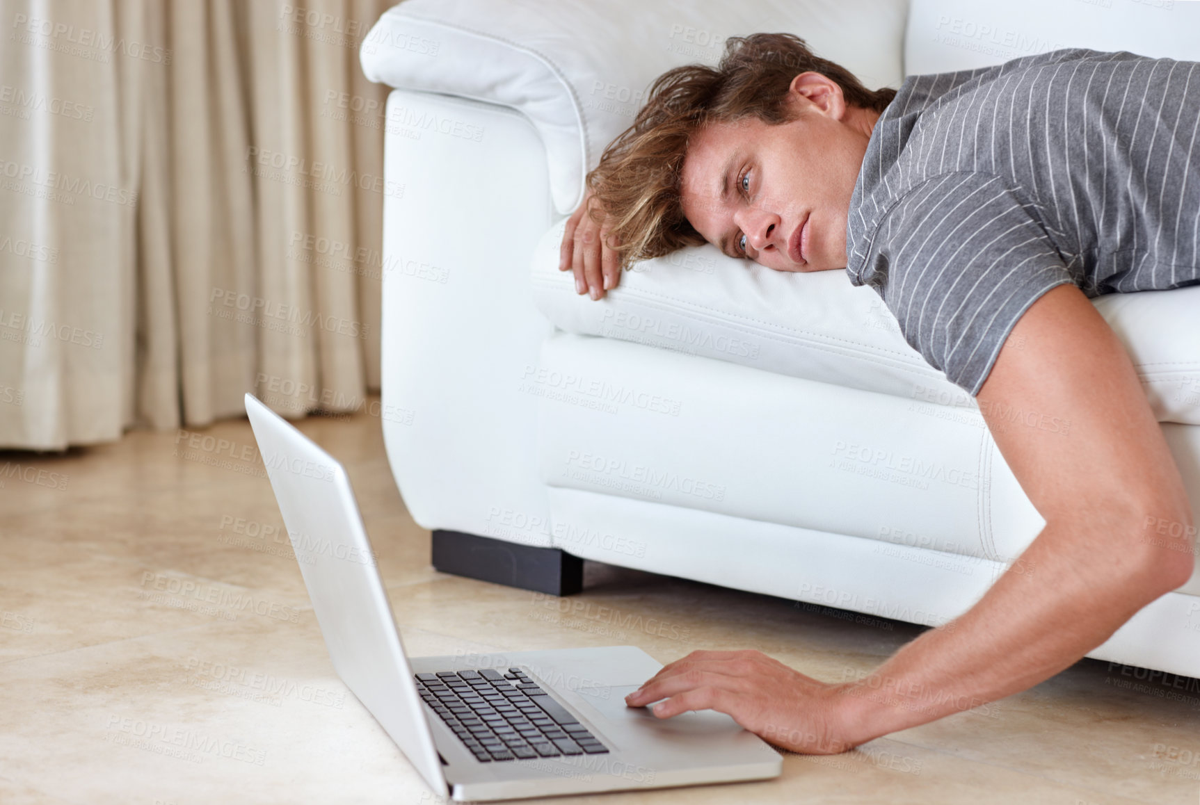 Buy stock photo A young man lying on his couch with his hand resting on his laptop's keyboard