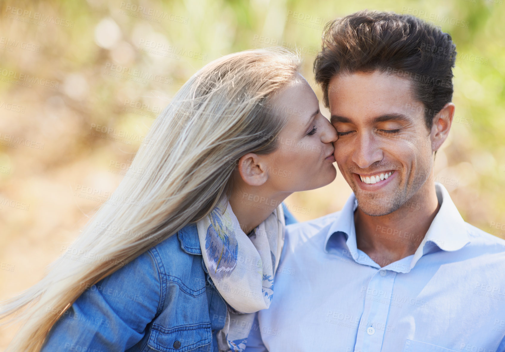 Buy stock photo Happy couple, kiss and cheek in nature for love, bonding or support in relax for outdoor affection. Face of young woman and man smile for embrace, intimacy or romance in forest or woods together