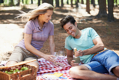 Buy stock photo Couple, picnic and champagne in nature with love, romantic celebration and summer date on valentines day. Young people with food, fruits and bottle with wine glasses in woods or forest on anniversary