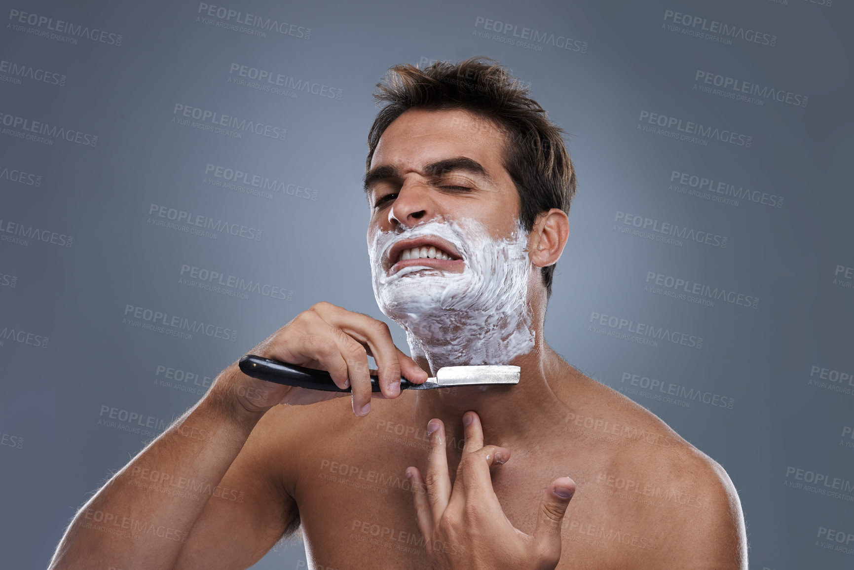 Buy stock photo Man, shaving and razor with stress in studio for grooming, skincare and wellness with pain by grey background. Person, model and annoyed with beard, facial hair removal and cream for cosmetic change