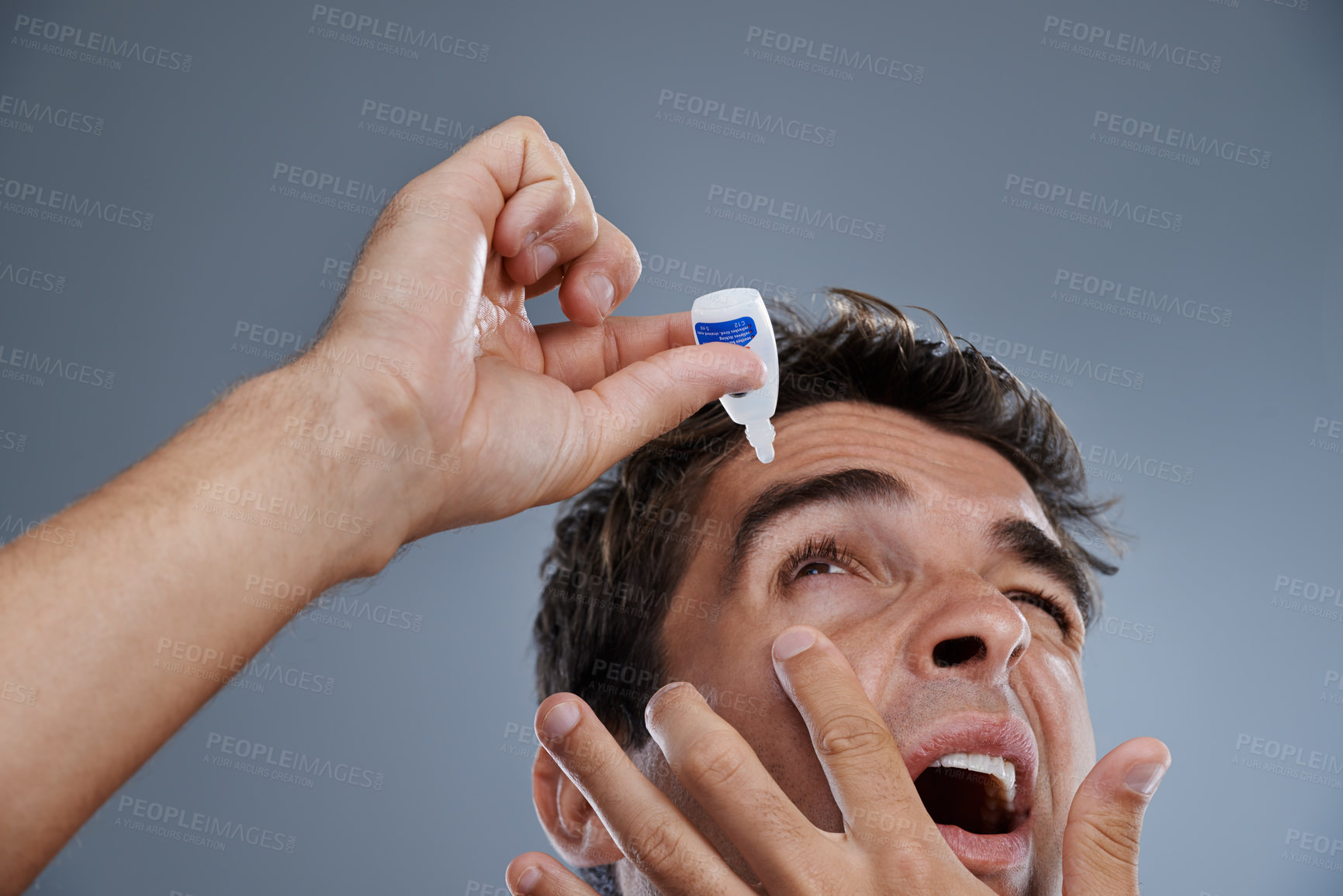 Buy stock photo Studio shot of a young man putting drops into his eye