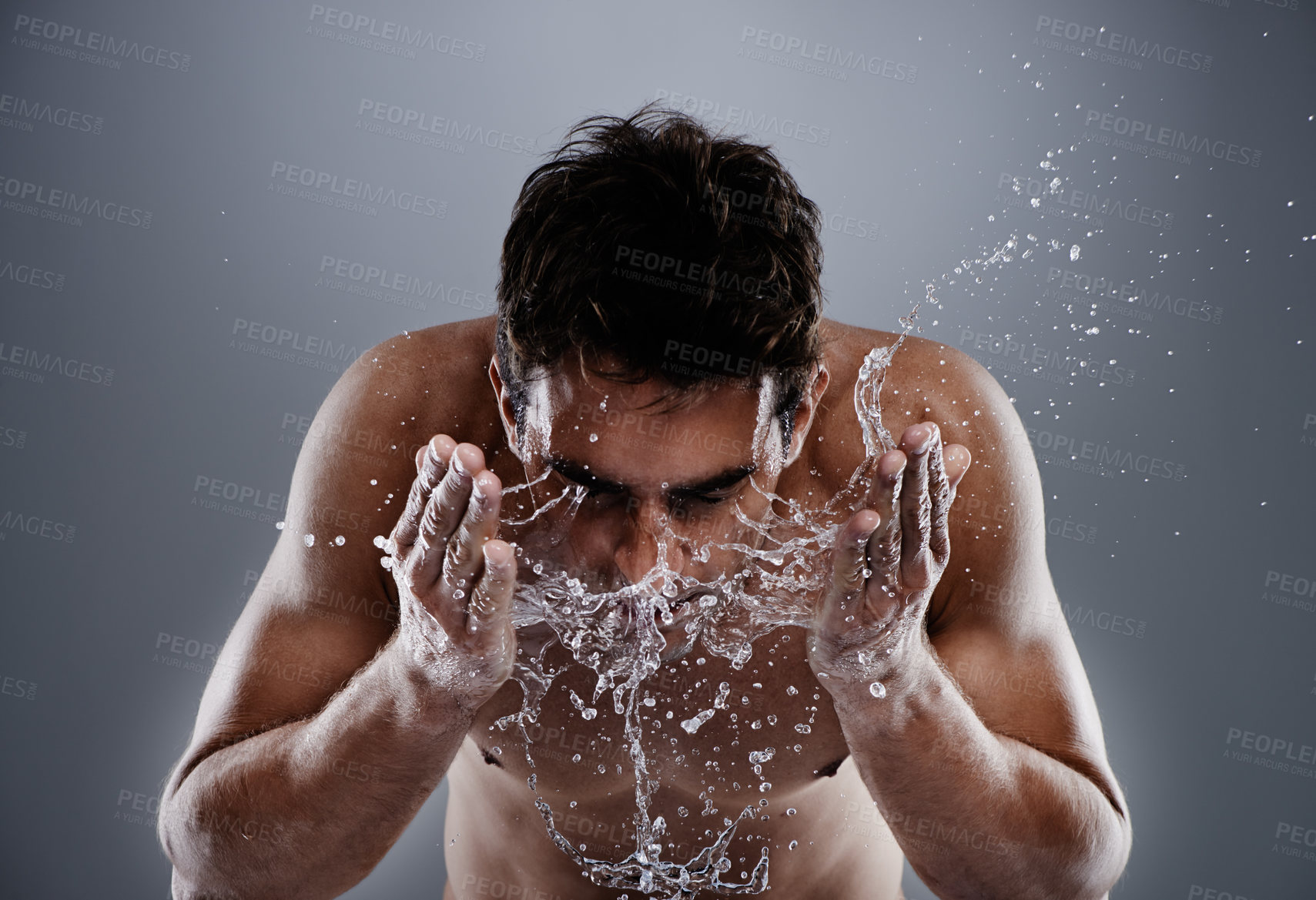 Buy stock photo Water drops, splash and man cleaning face for bathroom routine, dermatology cleanse or beauty treatment for skincare. Studio, moisture and model facial wash, hygiene and grooming on grey background