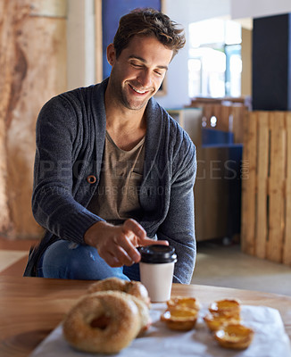 Buy stock photo Shot of a handsome young man sitting in a cafe and reaching for his coffee