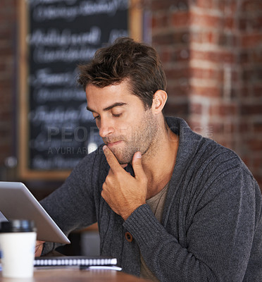 Buy stock photo A young man working on a digital tablet in a coffee shop