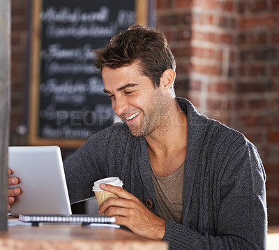 Buy stock photo A young man working on a digital tablet holding a coffee in a restaurant