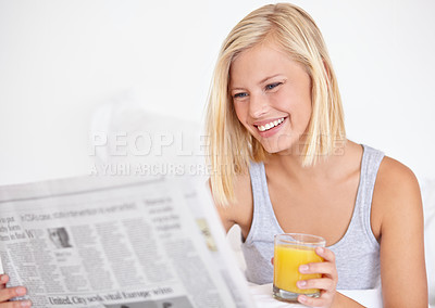 Buy stock photo A pretty young woman reading the newspaper in bed and enjoying a glass of OJ